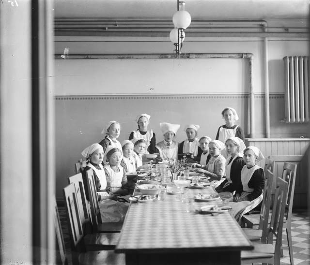 Skolk&ouml;ket 1912. Unga flickor samlade kring bordet. Skolk&ouml;ksundervisning i folkskolan, V&auml;stra skolan, Esl&ouml;v. L&auml;rarinnan hette Gerda Gr&ouml;nvall. K&auml;lla: Esl&ouml;vs kommuns bildarkiv, F&ouml;jers foto.