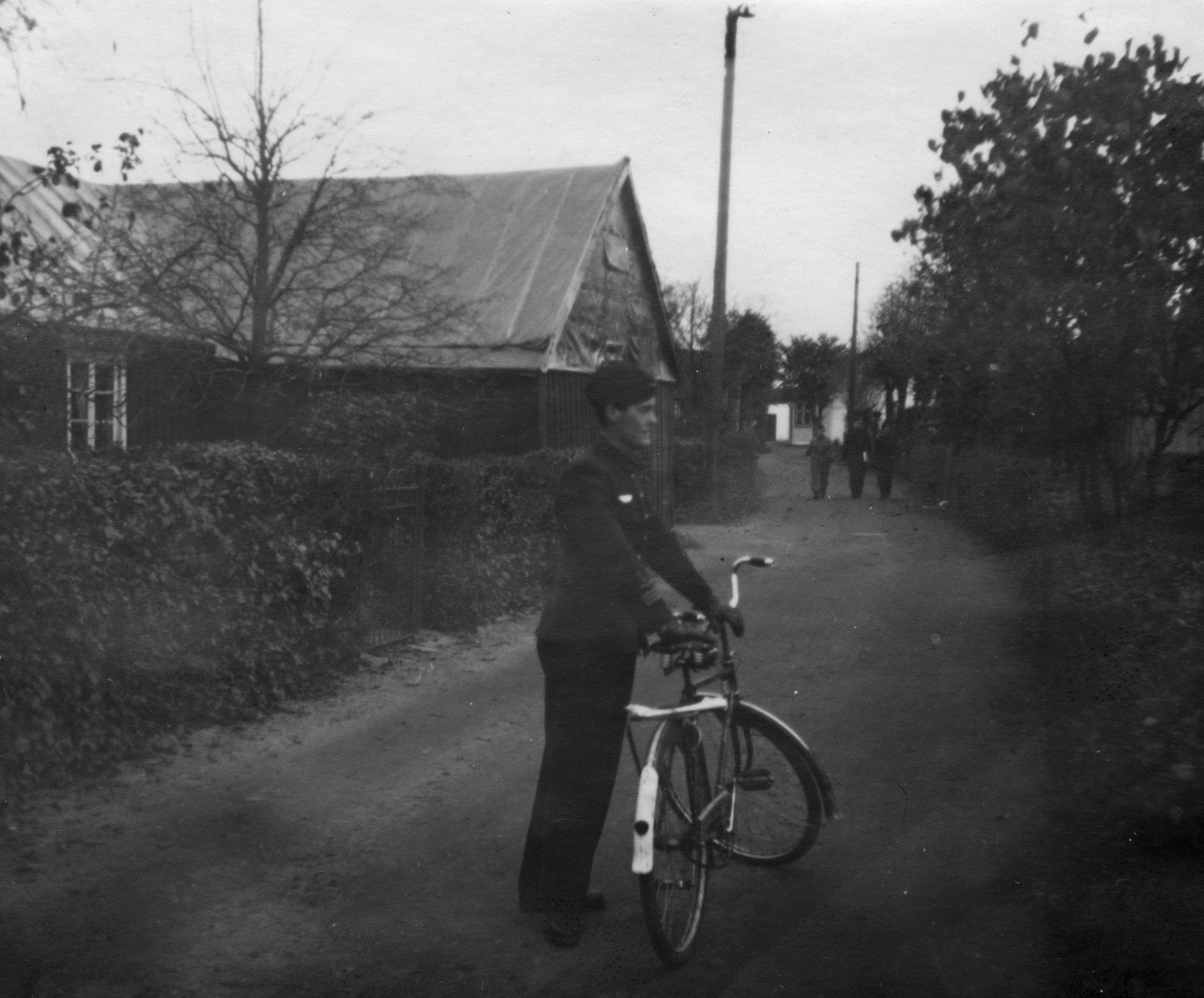 Motiv: En flygsoldat st&aring;r med cykel p&aring; en gata i Esl&ouml;v, 1943. Ur Kurt Edenstams album 'Minnen fr&aring;n Min kommistid 1940-1944'. Edenholm var stationerad p&aring; Krigsflygskolan F 5 samt F 9. Bildtext fr&aring;n albumet: "Allt &auml;r sig likt. Esl&ouml;v 1943". Tillh&ouml;r Flygvapenmuseums bildarkiv.