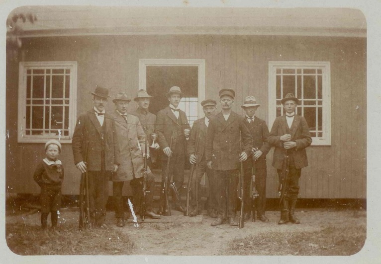 Skyttepaviljongen intill Tegelbruket. Marieholms skyttef&ouml;rening startade &aring;r 1900. Mannen i plommonstop, f&auml;rgm&auml;stare B&auml;ckstr&ouml;m sedan landstingsman Anton Hultgren. De tv&aring; i "sk&auml;rmm&ouml;ssor", t.v. fabrik&ouml;r Ad. Lundkvist i H&aring;stensl&ouml;v och tegelm&auml;stare N. J. Lindh.