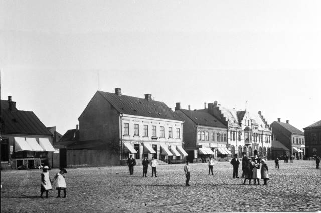 Fotot är taget i början av 1900-talet. Torget mot östra sidan längs Köpmansgatan. De affärer som då fanns är räknat från vänster: C Aug Asks speceriaffär, Ella Rosenqvists Mode, juvelerare Aug Lundström, samt J E Jönssons hatt- och mössaffär. Föjers Foto